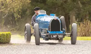 Ein Mann in einem schwarzen Hut fährt einen blauen Bugatti Type 35 über einen Schotterweg.