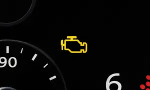 Gelbes Motorzeichen leuchtet auf dem Armaturenbrett eines Autos auf. Es ist Zeit, die Werkstatt zu besuchen.
