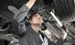 Mechaniker bei der Inspektion eines Autos. Er leuchtet mit einer Lampe unter das Fahrzeug, um alle Teile zu prüfen.
