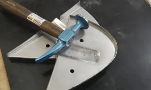 Karosserie Werkzeug für Oldtimer: Ein Ausbeul-Pinnhammer liegt auf einem Blechteil, bereit für die Restaurierung.
