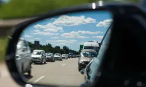 Autofahrer stellt den spiegel richtig ein, um den Verkehr auf der Autobahn zu sehen. Blauer Himmel mit Wolken spiegelt sich im Spiegel.