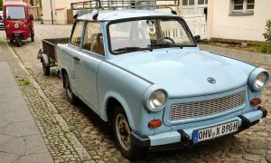 Hellblauer Trabant Kübelwagen mit Anhänger, Baujahr und Zulassung erkennbar.