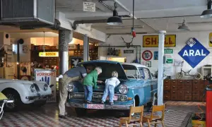 Familie bei der Oldtimer-Restauration eines blauen Opels. Der Vater erklärt den Kindern den Motorraum.