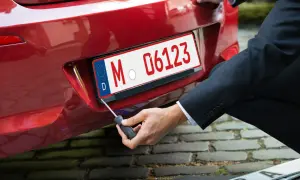 Mann schraubt Kennzeichen an rotes Auto. So bekommt man ein rotes Kennzeichen für Überführungsfahrten.