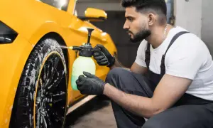 Mann mit Handschuhen sprüht Reinigungsmittel auf gelbe Felgen eines Autos.