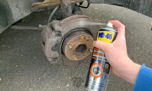 Hand sprüht Bremsenreiniger auf eine Bremsscheibe. Die Anwendung von Bremsenreiniger ist wichtig für die Wartung.