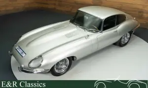 Silberner Jaguar E-Type Coupé mit Speichenrädern und Holzlenkrad, ein zeitloser Klassiker.