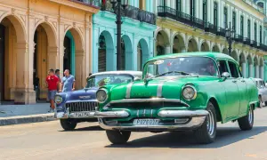 Grüne und blaue Oldtimer fahren auf einer Straße in Havanna. Diese Autos sind ein Symbol für die Geschichte und den Charme der Stadt, die man oft bei einem **oldtimer importieren** erleben kann.
