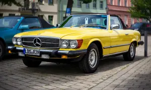 Ein leuchtend gelber Mercedes-Benz SL Roadster, ein Klassiker unter den retro autos, parkt auf einem Kopfsteinpflasterplatz.