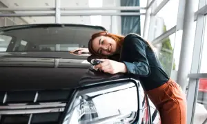 Glückliche Frau mit Autoschlüssel lehnt sich an ihren neuen Wagen. Der Traum vom Auto aus Belgien importieren wird wahr.