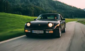 Dunkelroter Porsche mit Klappscheinwerfer fährt auf kurviger Landstraße durch grüne Hügel.