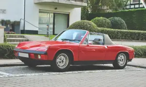 Roter Porsche 914 Roadster parkt vor einem modernen Haus mit gepflegten Hecken.