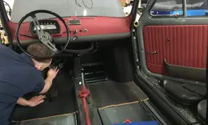 Der Mann arbeitet am fiat 500 oldtimer innenraum. Rote Türverkleidung und Armaturenbrett sind sichtbar.
