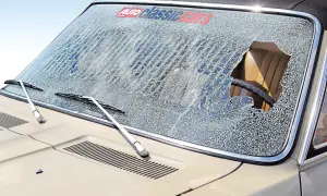 Zerbrochene Frontscheibe eines Oldtimers, bereit für den Wechsel. Ein großes Loch offenbart den Innenraum.