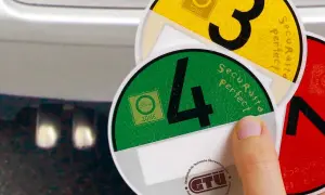 Umweltplaketten für Umweltzonen in Europa. Eine Hand hält grüne und gelbe Plaketten mit den Zahlen 4 und 3.