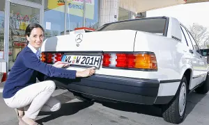 Frau befestigt ein H-Kennzeichen an einem weißen Mercedes. Was kostet ein H Kennzeichen?