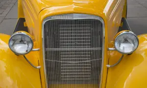 Nahaufnahme eines gelben Oldtimers mit glänzender Lackierung. Der Kühlergrill und die runden Scheinwerfer sind gut sichtbar.