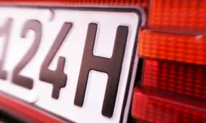 Nahaufnahme eines Nummernschilds mit der Aufschrift "124H". Daneben ist ein rotes Rücklicht zu sehen. Vielleicht eine Geschwindigkeitsbegrenzung?
