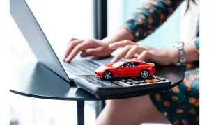 Rote Spielzeugauto auf Taschenrechner, während Hände auf Laptop tippen. Möglicherweise Vorbereitung für die auto abmelden.