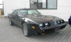 Schwarzer Pontiac Trans Am, ein klassisches Muscle Car mit Adler-Grafik auf der Motorhaube, steht auf einem gepflasterten Hof.
