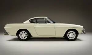 Ein cremefarbener Volvo P1800 Coupé steht im Profil, seine eleganten Linien und Chromdetails glänzen.