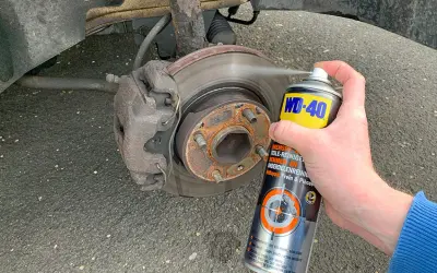 Hand sprüht Bremsenreiniger auf eine Bremsscheibe. Die Anwendung von Bremsenreiniger ist wichtig für die Wartung.