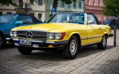 Ein leuchtend gelber Mercedes-Benz SL Roadster, ein Klassiker unter den retro autos, parkt auf einem Kopfsteinpflasterplatz.