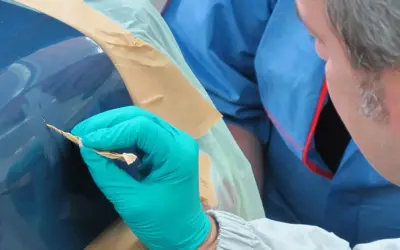 Mann mit Handschuh entfernt Rost von Autolack. Sorgfältige Arbeit, um das Auto entrosten.