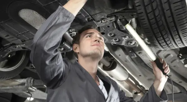 Mechaniker bei der Inspektion eines Autos. Er leuchtet mit einer Lampe unter das Fahrzeug, um alle Teile zu prüfen.