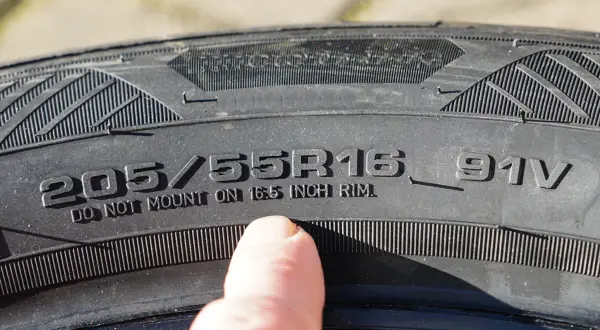 Ein Finger zeigt auf die Reifengröße 205/55R16, um die Zoll-Angabe abzulesen.