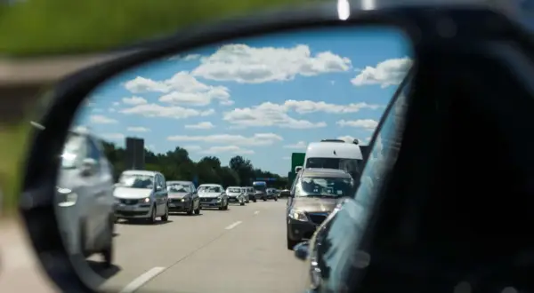 Autofahrer stellt den spiegel richtig ein, um den Verkehr auf der Autobahn zu sehen. Blauer Himmel mit Wolken spiegelt sich im Spiegel.