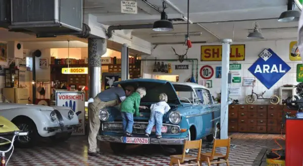 Familie bei der Oldtimer-Restauration eines blauen Opels. Der Vater erklärt den Kindern den Motorraum.
