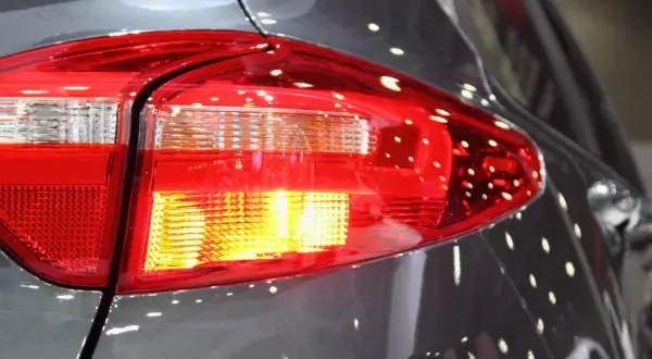 Rücklicht eines Autos, der Blinker blinkt schnell. Reflektionen auf dem grauen Lack.