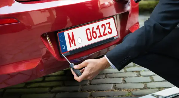 Mann schraubt Kennzeichen an rotes Auto. So bekommt man ein rotes Kennzeichen für Überführungsfahrten.