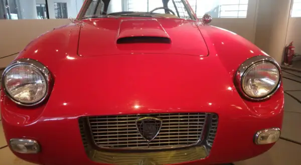 Vorderansicht eines roten italienischen Oldtimers mit Lancia-Logo im Kühlergrill.