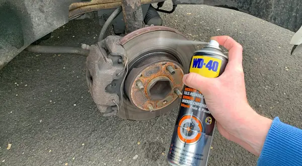 Hand sprüht Bremsenreiniger auf eine Bremsscheibe. Die Anwendung von Bremsenreiniger ist wichtig für die Wartung.