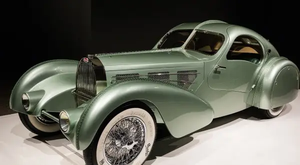 Ein alter Bugatti in pastellgrün, ein Meisterwerk der Automobilgeschichte mit geschwungenen Linien und Speichenrädern.