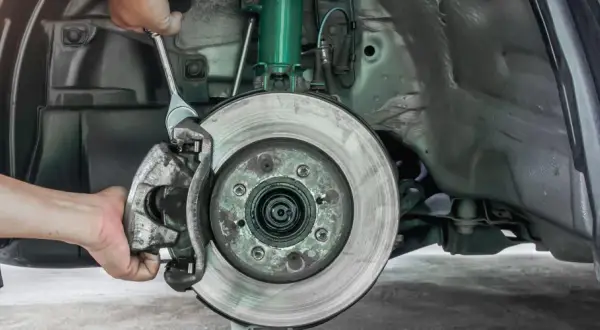 Mechaniker wechselt Bremssattel. Informieren Sie sich über die Bremsen wechseln Kosten für Ihr Fahrzeug.