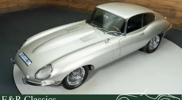 Silberner Jaguar E-Type Coupé mit Speichenrädern und Holzlenkrad, ein zeitloser Klassiker.