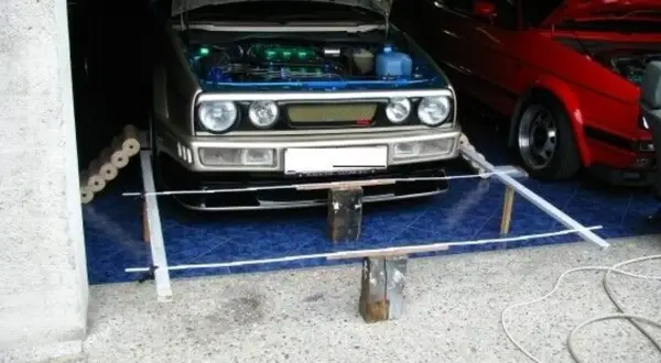 Selbstgemachte Achsvermessung: Ein silberner VW Golf mit geöffneter Haube steht bereit. Daneben ein roter Wagen.