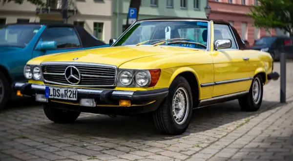 Ein leuchtend gelber Mercedes-Benz SL Roadster, ein Klassiker unter den retro autos, parkt auf einem Kopfsteinpflasterplatz.