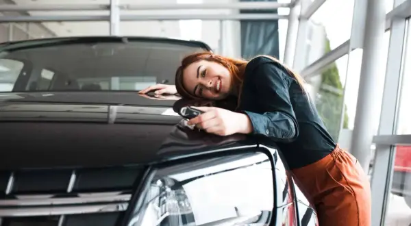 Glückliche Frau mit Autoschlüssel lehnt sich an ihren neuen Wagen. Der Traum vom Auto aus Belgien importieren wird wahr.