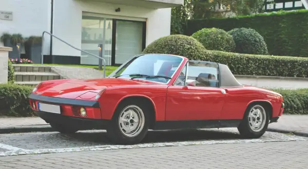 Roter Porsche 914 Roadster parkt vor einem modernen Haus mit gepflegten Hecken.