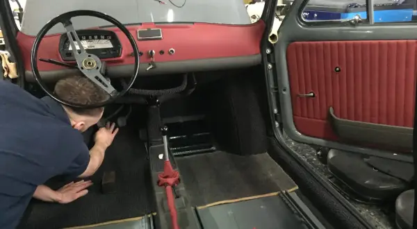 Der Mann arbeitet am fiat 500 oldtimer innenraum. Rote Türverkleidung und Armaturenbrett sind sichtbar.