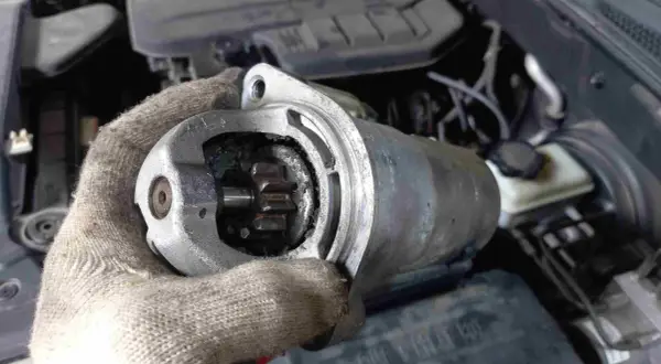 Defekter Anlasser Mercedes: Werkzeug in Handschuh hält ausgebauten Anlasser mit sichtbarem Ritzel. Kosten für Reparatur im Blick.