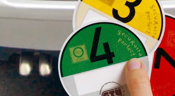 Umweltplaketten für Umweltzonen in Europa. Eine Hand hält grüne und gelbe Plaketten mit den Zahlen 4 und 3.