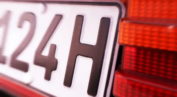 Nahaufnahme eines Nummernschilds mit der Aufschrift "124H". Daneben ist ein rotes Rücklicht zu sehen. Vielleicht eine Geschwindigkeitsbegrenzung?