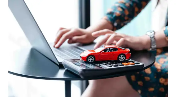 Rote Spielzeugauto auf Taschenrechner, während Hände auf Laptop tippen. Möglicherweise Vorbereitung für die auto abmelden.