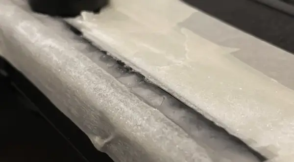 Detailaufnahme: Riss in einem Bakelit-Teil, der mit Klebeband abgedeckt ist. Ein schwarzer Drehknopf ist im Hintergrund zu sehen. Hier wird Bakelit reparieren.