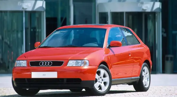 Roter Audi A3 vor einem modernen Gebäude. Ein Klassiker, der bald das Youngtimer Kennzeichen tragen darf.